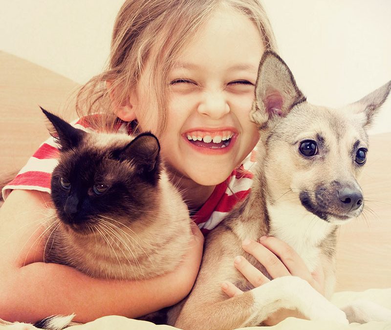 Criança branca feliz abraçando um gato e um cachorro.